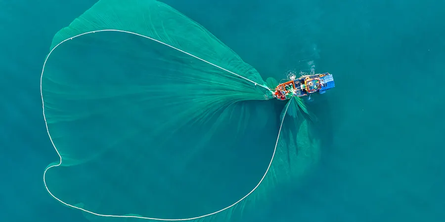 UK pension consolidation for Expats Blog Image 01 Aerial shot of a fishing boat casting a wide net over calm blue water, symbolising how expats can gather scattered UK pensions into one consolidated plan.